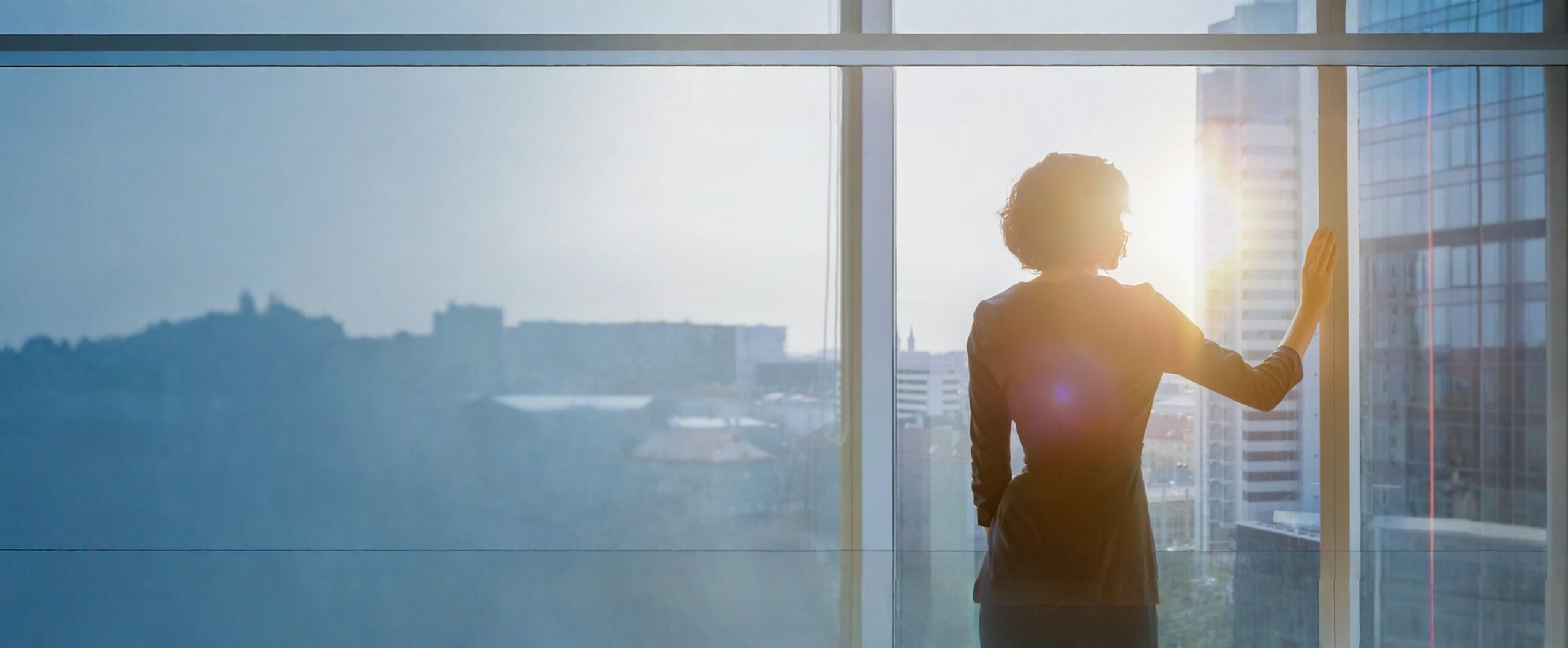 Eine Frau blickt aus einem modernen Büro auf die Stadt – Perspektiven für neues Arbeiten
